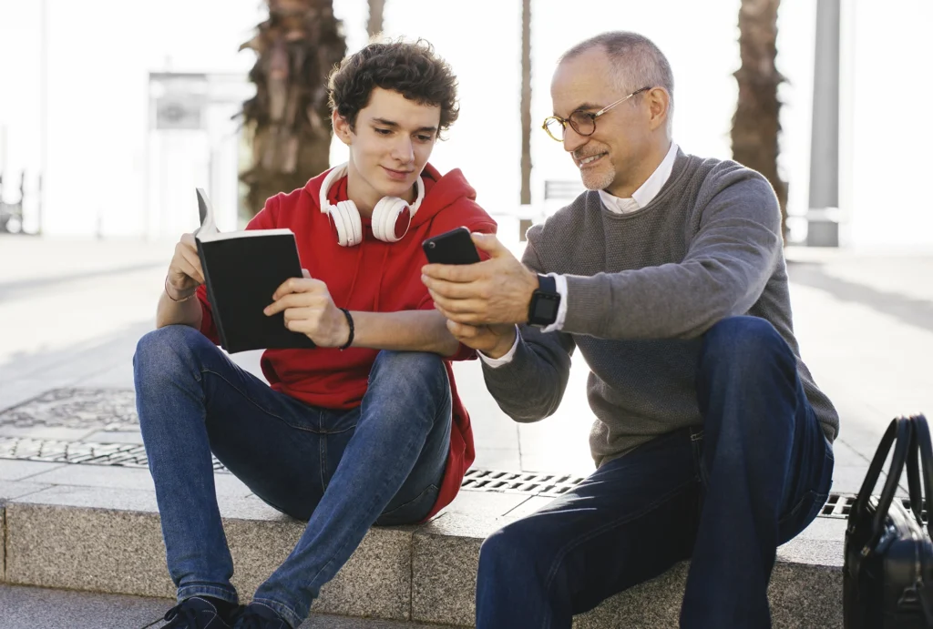 Father and son sitting together looking at financial information on mobile devices