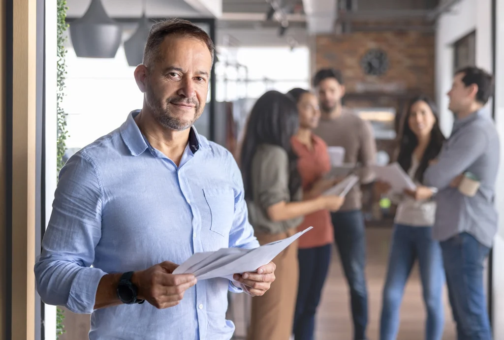 business owner in office holding papers with employees in the background