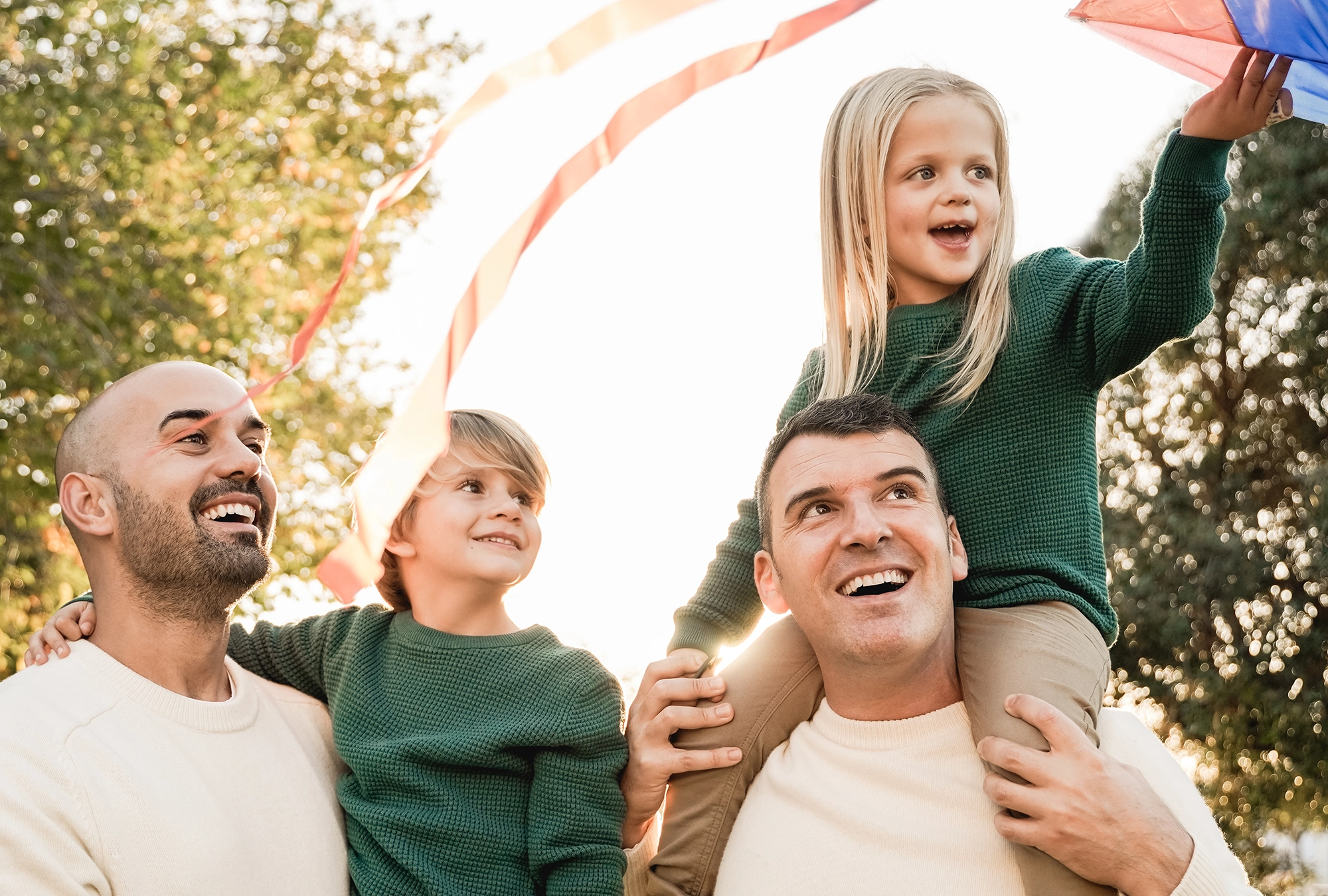 Male gay couple carrying their kids outside and having fun